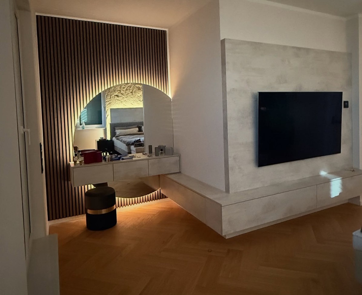 Schminktisch vor Lamellenwand mit halbrundem Spiegel, daneben TV-Wand mit Lowboard